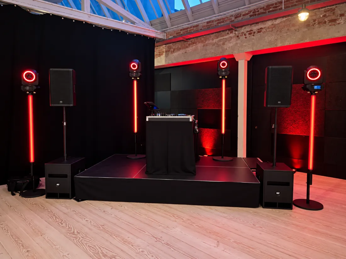 DJ-scene med sort podie, højttalere og røde lyssøjler i et festlokale